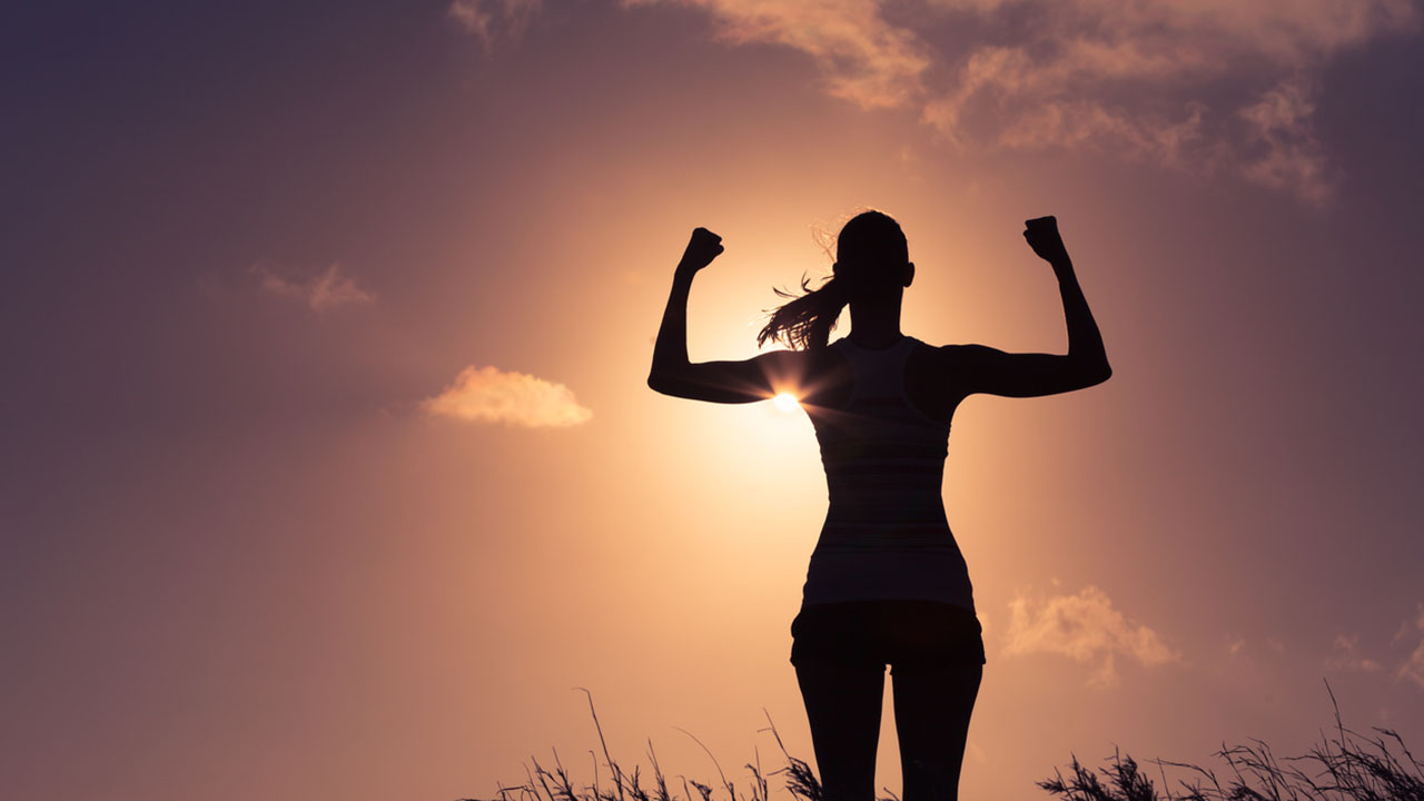 Silhouette of a woman with arms in the air and the sun behind her