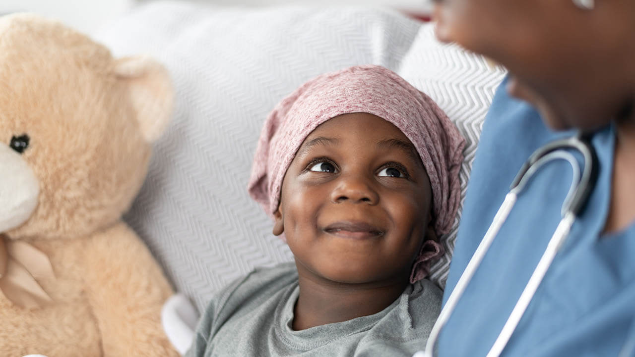 Black girl with cancer in a hospital bed smiling at a nurse