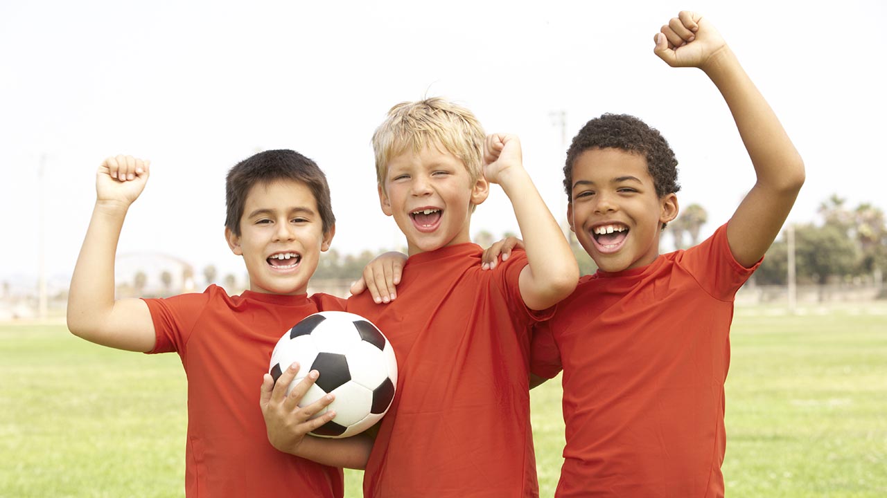 Three boys cheering in soccer gear and holding a ball