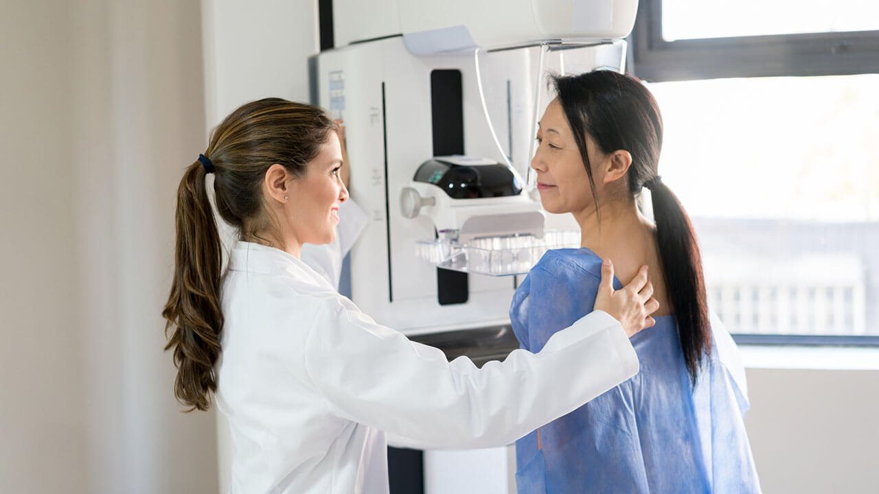 Middle age women standing in front of a mammogram machine with a female technician