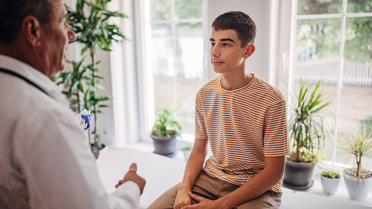 Tennager boy on medical table talking to middle age male doctor