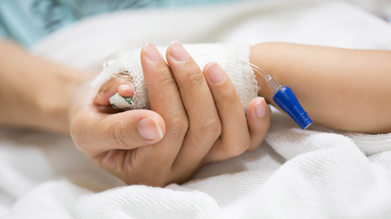 Parent holding child's hand in hospital bed