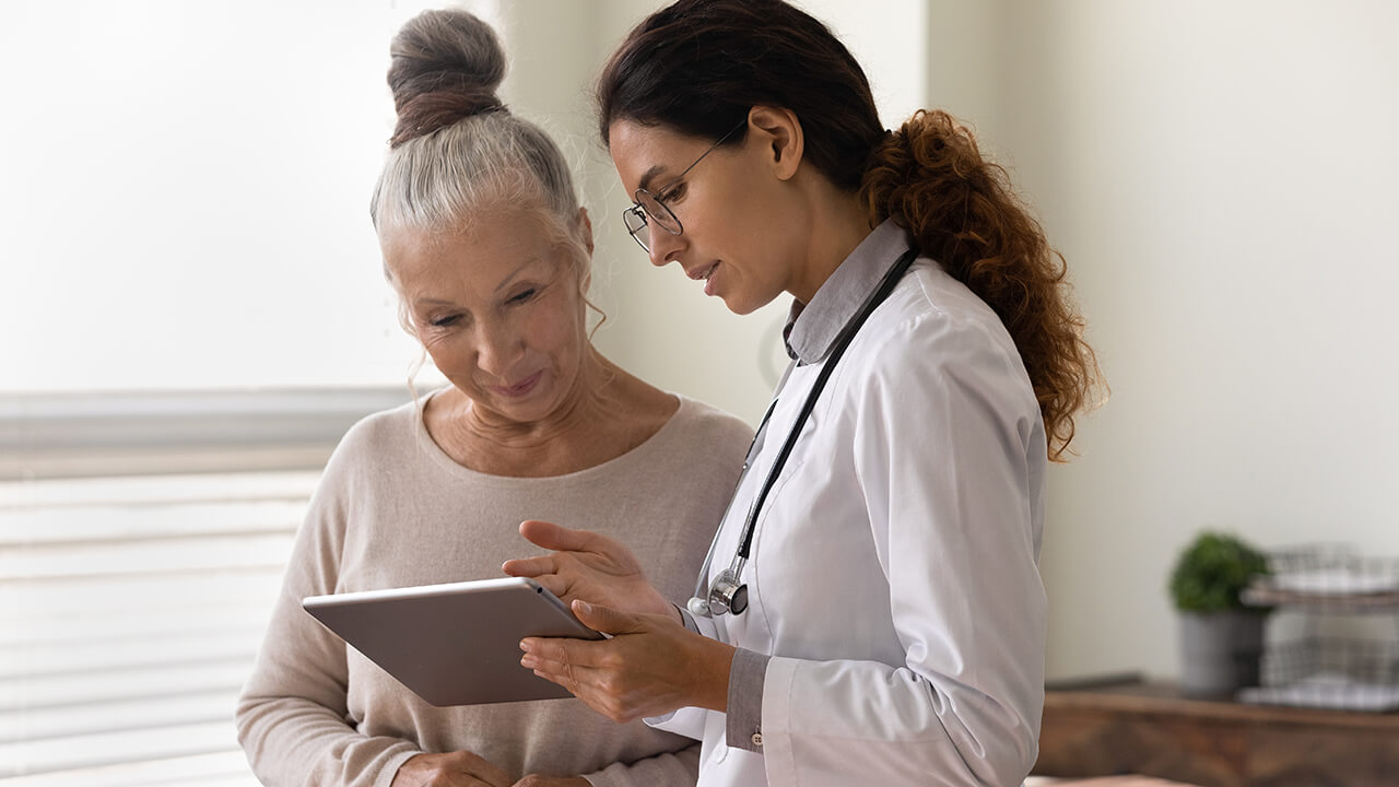 female doctor talking to elderly female patient while showing her a tablet