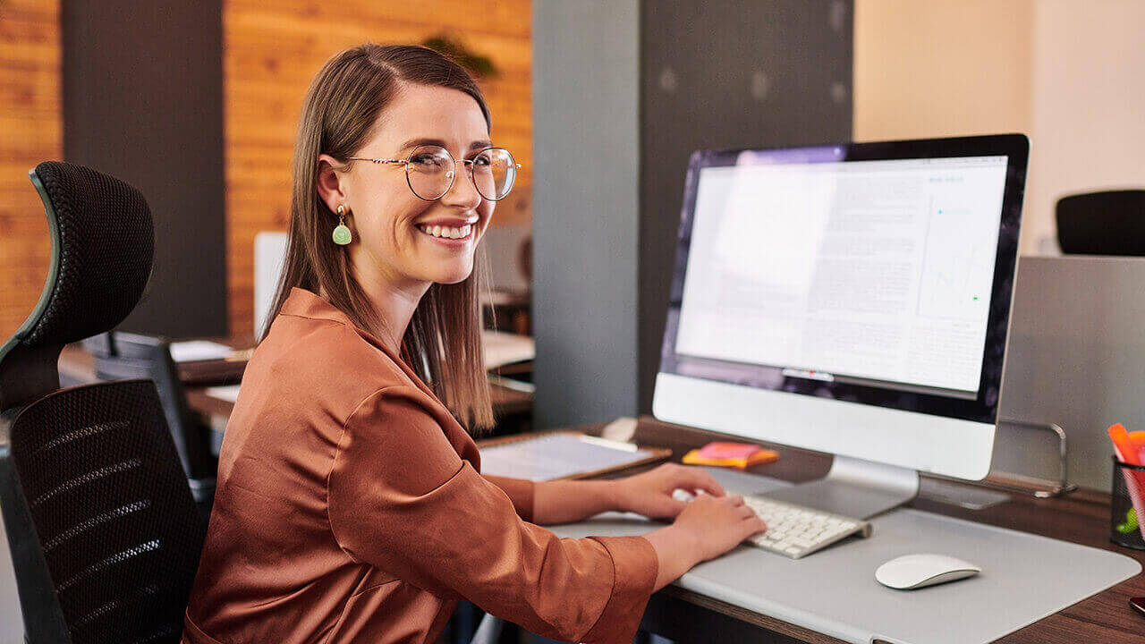 Young woman typing on MAC computer while smiling