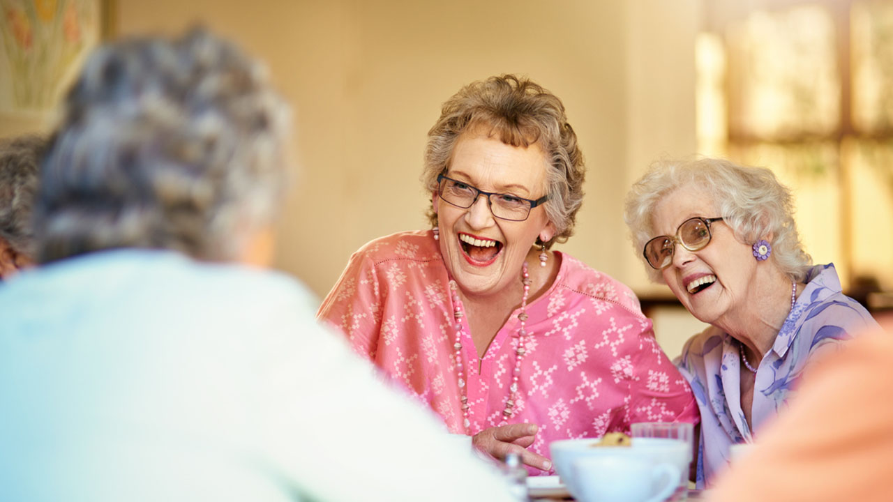 Three senior women laughing at a kitchen table