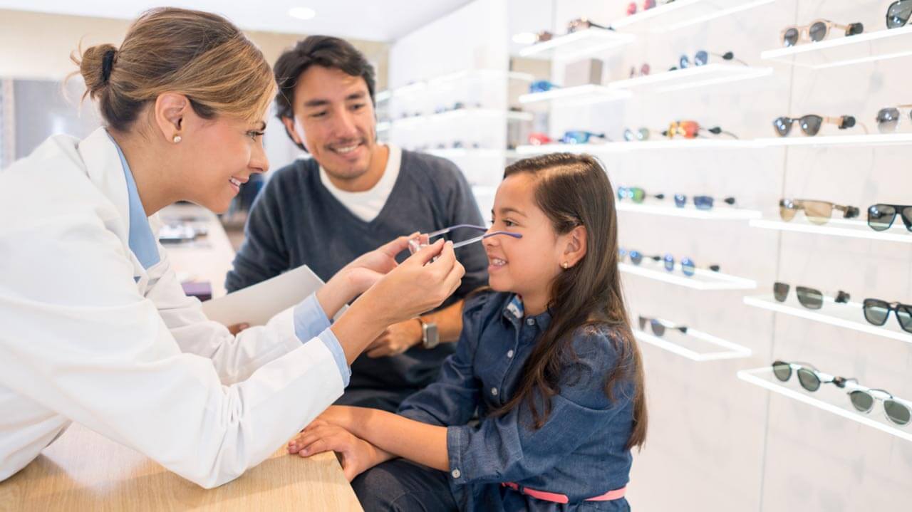 Female Ophthalmologist placing glasses on young girl's face