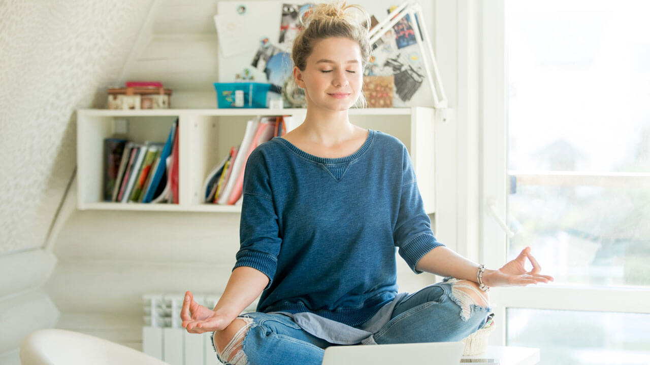 Young woman sitting with legs crossed on a bed with eyes closed