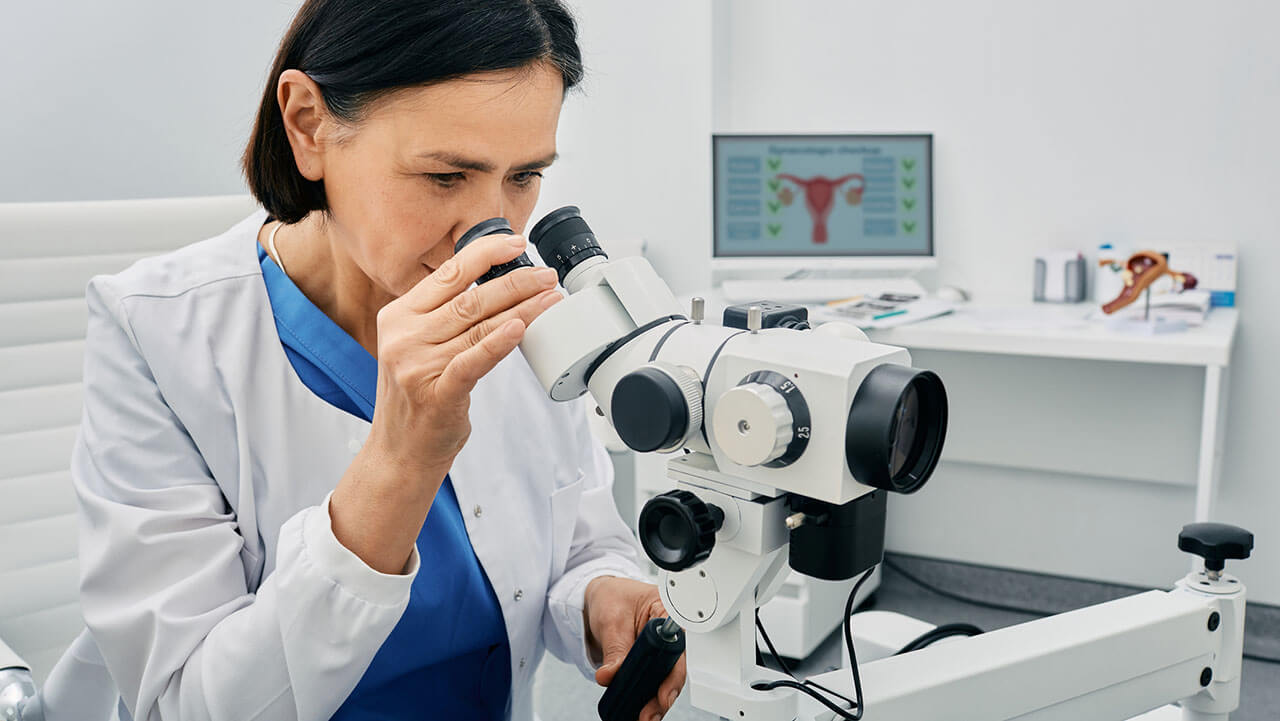 Experienced gynecologist woman sitting near colposcopy in her gynecological office.