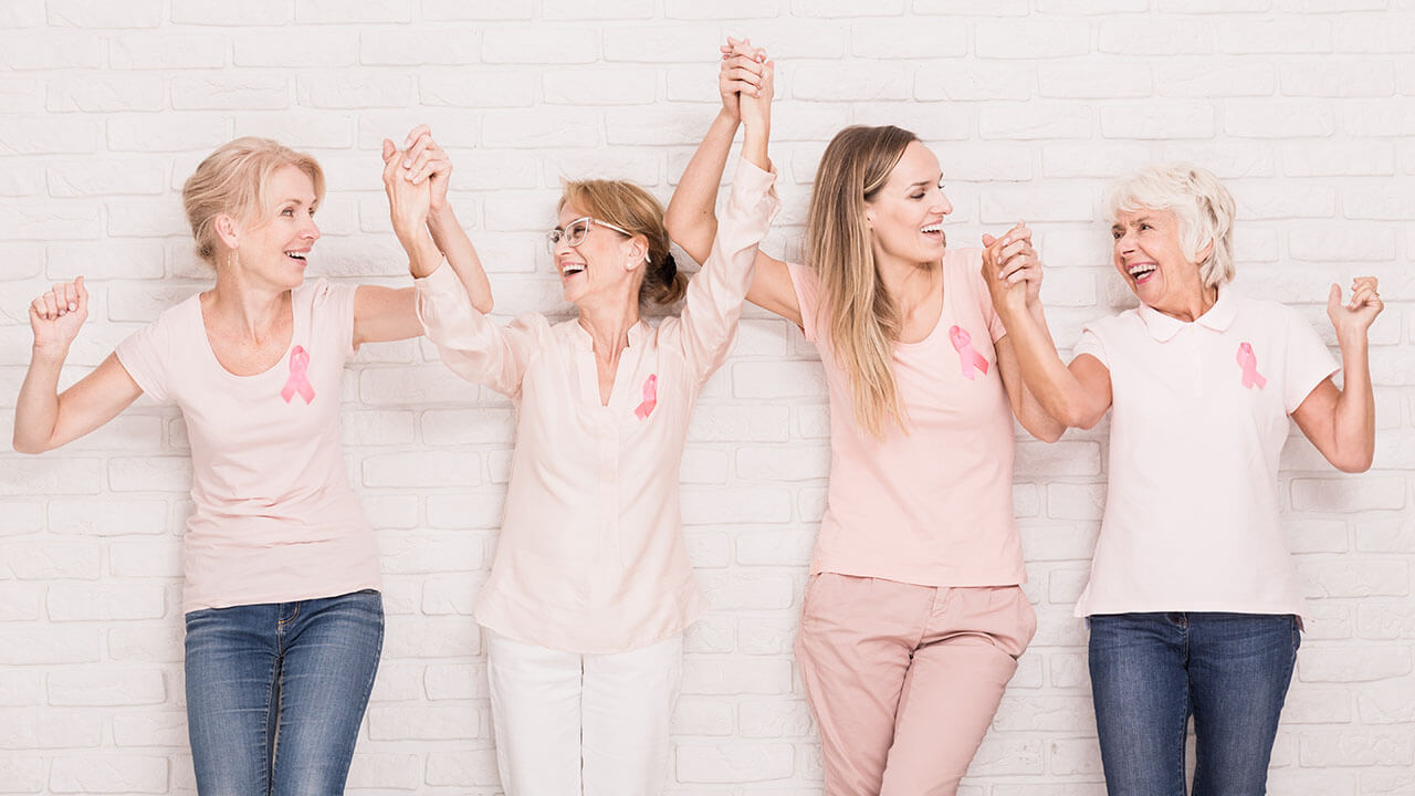 Four women of different ages wearing pink clothes and holding hands