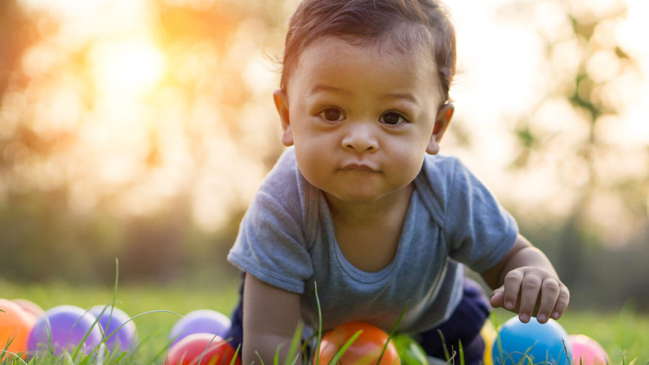 small child crawling on grass outdoors with toys around him