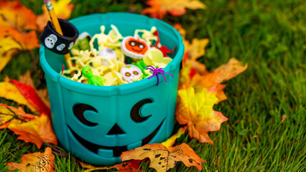Teal pumpkin bin full of Halloween candy surrounded by leaves on the ground